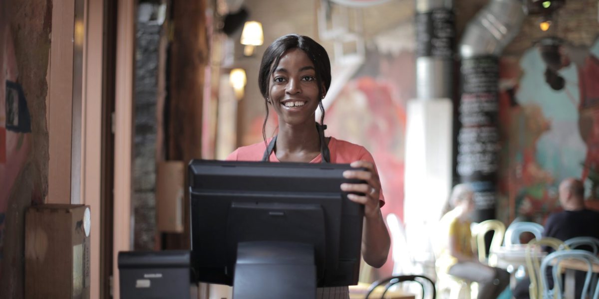 Positive young woman in uniform smiling while standing at counter desk in cafe