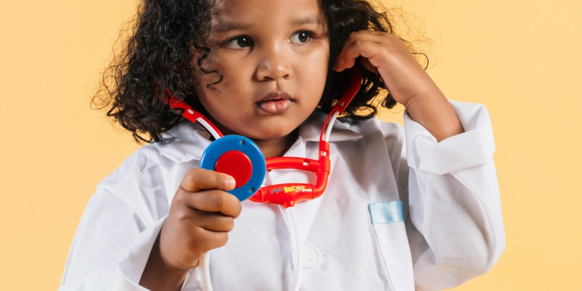 Little black girl in medical robe playing with toy stethoscope