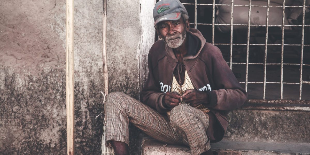 Full body mature poor Asian male in worn out clothes sitting on shabby grunge stair in backyard and looking at camera wistfully